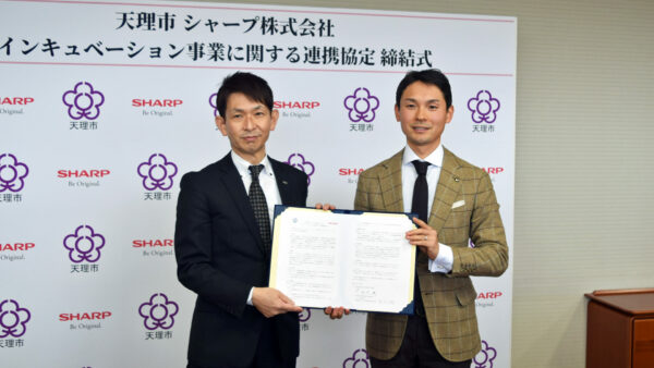 天理市庁で行われた連携協定締結式にて、サインした連携協定書を持つ 当社常務執行役員 研究開発事業本部長 種谷 元隆（左）と天理市長 並河 健 氏